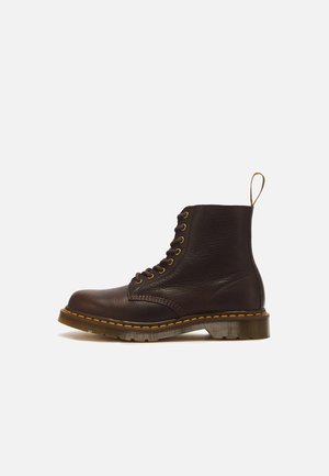Schwarzer Leder-Schnürstiefel mit gelben Nähten und einer Zuglasche auf einer braunen durchsichtigen Sohle, von der Seite auf weißem Hintergrund dargestellt.
