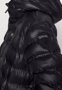 Černá péřová bunda se lesklou prošívanou texturou, vysokým límcem a vyšívanou nášivkou s logem na rameni.