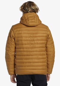 Padded bunda v teplej hnedej farbe, so horizontálnym prešívaním, kapucňou a elastickými manžetami. Hladká textúra, ľahká tkanina a bez viditeľného hardvéru.