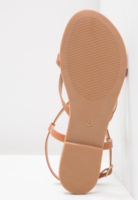 Tan strappy sandal with a rubber sole, featuring horizontal grooves for grip and a size mark of 37 on the bottom.
