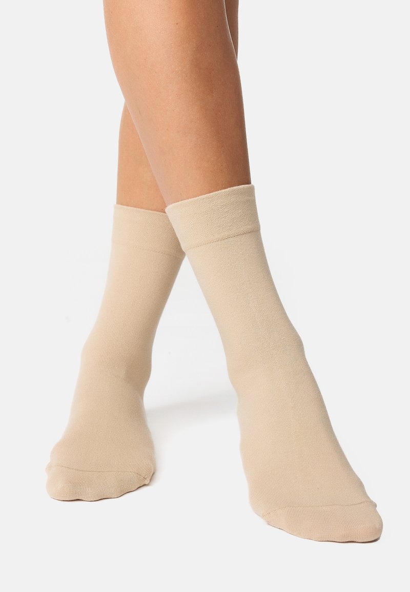 Beige strømper i crew-længde lavet af et blødt, strækbart materiale; ribbet kant foroven, glat tekstur og minimalistisk design.