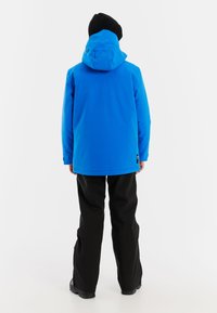 Blaue isolierte Jacke mit Kapuze, verfügt über eine glatte Textur und wird mit schwarzen wasserfesten Hosen und Stiefeln kombiniert.