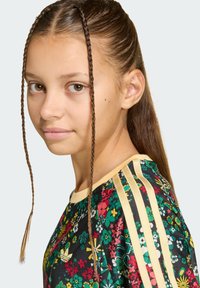 Αθλητικό τοπ με λουλουδάτο σχέδιο που παρουσιάζει ζωντανά, πολύχρωμα λουλούδια σε μαύρο φόντο, με αποχρώσεις ανοιχτού κίτρινου στις ραφές των ώμων.