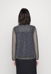 Blusa trasparente blu navy con un motivo a pois, maniche lunghe e orlo arrotondato. Il retro presenta un design semplice con dettagli minimi.