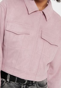 Kort jacka i mjuk rosa imitationsläder, med krage, två bröstfickor och en strukturerad design. Texturerad yta, minimalistisk stil.