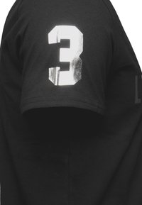 Czarny bawełniany t-shirt z metalicznym srebrnym nadrukiem „3” na lewym rękawie. Gładka faktura z klasycznym dekoltem typu crew neck.