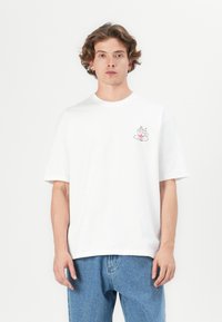 White cotton t-shirt featuring a small graphic of a steaming cup on the left chest, with loose-fitting short sleeves and a crew neck.