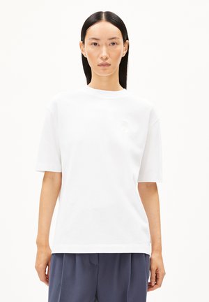 Camiseta de algodón blanca con mangas cortas y escote redondo. Presenta un sutil detalle de logo en la parte izquierda del pecho. Corte simple y relajado.