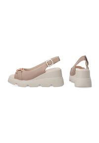 Beige slingback wedge sandaaltjes met een gestructureerde bovenkant, verstelbare gesp en een stevige witte zool. Voorzien van een decoratieve metalen accent.