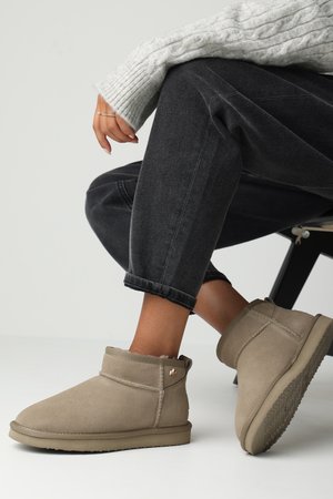 Bottines en suède beige à la cheville, avec un intérieur doux, un revers roulé et une semelle en caoutchouc texturée. Comprend un petit accent métallique.