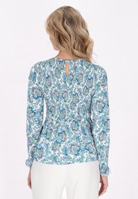 Blusa a maniche lunghe in motivo floreale azzurro chiaro con retro smock, dettaglio a occhiello nel collo e maniche arricciate. Realizzata in tessuto leggero.
