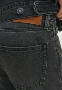 Svarta denimjeans med en strukturerad yta, bakfickors sömnad och en beige lädervårdsetikett sydd i midjan.