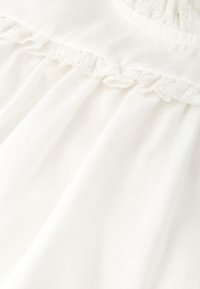 Tejido de algodón blanco con un delicado borde de encaje y textura fruncida. Presenta suaves pliegues fluidos para un aspecto ligero y etéreo.