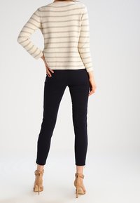 Maglione chiaro in crema con strisce orizzontali beige, abbinato a pantaloni slim scuri e scarpe con tacco nude. Vestibilità sartoriale e tessuto lavorato.