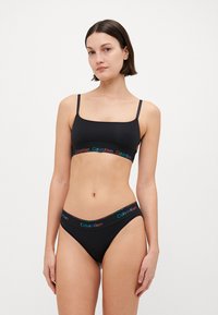 Črn bombažni modrček in hlačke z tankimi naramnicami, ki imajo večbarvno Calvin Klein logotipno elastiko. Gladka tekstura in prilegajoč dizajn.