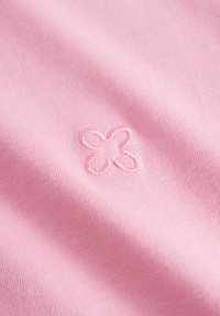 Roze stof met een gladde textuur heeft in het midden een klein geborduurd bloemenachtig ontwerp, dat de eenvoud en ambachtelijkheid benadrukt.