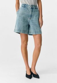 Shorts in denim di colore azzurro con vita alta, due tasche laterali e orlo grezzo. Abbinati a scarpe con tacco nero a punta.