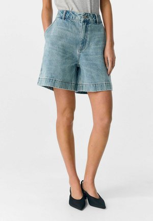 Shorts en jean bleu clair à taille haute, avec deux poches sur les côtés et un ourlet brut. Assortis à des escarpins noirs à bout pointu.