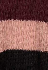 Pull en tricot présentant trois bandes horizontales : bordeaux foncé, rose pâle et noir profond. La texture semble épaisse et chaude.