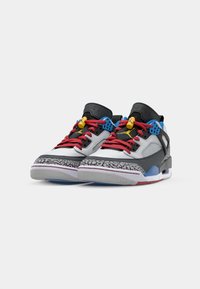 Grå og sorte sneakers med røde snørebånd, gule og blå accenter, tekstureret mellemsål og mønstret ydersål. Har Jordan-branding.