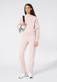 Lichtroze sweatshirt met ribbelige zoom, gecombineerd met bijpassende broek en een kleine mintgroene schoudertas met zwarte accenten. Witte sneakers.