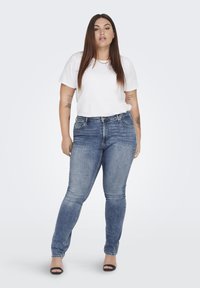 Vaqueros de mezclilla azul ajustados con un ligero estiramiento, diseño de cinco bolsillos y cremallera. Combinados con una camiseta blanca básica de cuello redondo.
