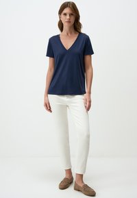 Marineblaues V-Ausschnitt-T-Shirt aus weichem Stoff, kombiniert mit weißen gerade geschnittenen Hosen und braunen Slippern. Schlichtes Design, kurze Ärmel und lässige Passform.