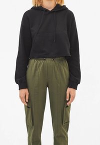 Svart avkortad hoodie med snoddar, kombinerad med olivgröna cargobyxor med sidofickor och resårmidja.