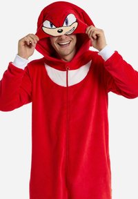 Red fleece onesie featuring a hood with a character face design, white accents, and a front zipper. Soft texture and casual fit.
