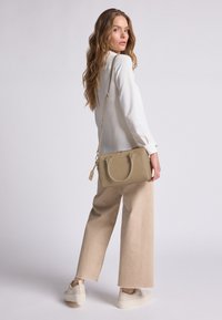Beige leren handtas met dubbele handvatten en een verstelbare schouderband. Soepele textuur, rechthoekige vorm, met subtiele stiksels en een bedel.