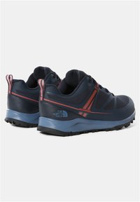 Zapatillas de trail en azul oscuro con materiales de malla y sintéticos, que cuentan con acentos rojos, suela de tracción y un cuello acolchado para mayor comodidad.