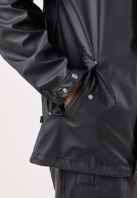 Czarna wodoodporna kurtka o gładkiej fakturze, z regulowanymi mankietami i detalami z zatrzaskami na bocznej kieszeni.