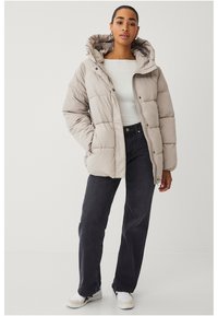 Giacca puffer beige chiaro con cappuccio, caratterizzata da cuciture a righe orizzontali, una zip frontale e bottoni a pressione. Indossata sopra una maglietta bianca e jeans scuri.