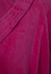 Fleece-Material in leuchtendem Pink, mit einer weichen, strukturierten Oberfläche und einem genähten Rand entlang des Kragens. Glattes und warmes Gefühl.
