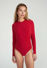 Body rosso a maniche lunghe realizzato in un morbido tessuto elasticizzato, con scollatura rotonda e gambe alte, progettato per un silhouette aderente.