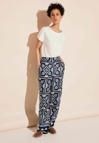 Marineblauwe wijdlopende broek met witte bloemmotieven, gemaakt van lichte stof. Gecombineerd met een casual wit T-shirt en bruine instappers.
