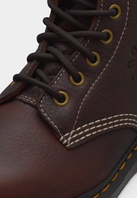 Κοντινό πλάνο ενός καφέ δερμάτινου μποτακιού με σκούρα κορδόνια περασμένα από μπρούτζινα οπτικά και διπλή λευκή ραφή κατά μήκος των ραφών.