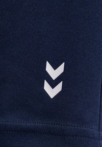 Granatowa tkanina o gładkiej fakturze z dwiema białymi, zwróconymi w dół chevronami. Wzór zawiera czysty szew u dołu.