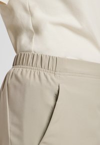 Beige broek met elastische taille, gemaakt van gladde stof, met zijzakken en een ontspannen pasvorm. De stof heeft een licht glanzende afwerking.