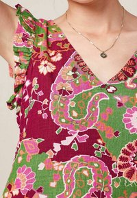 Tela colorida y estampada con una base burdeos profunda y diseños florales en rosa, verde, naranja y blanco. Cuenta con acentos de mangas con volantes.