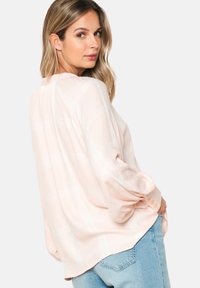 Light pink plaid blouse with long sleeves, made from a smooth fabric, featuring cuff buttons and a relaxed fit, paired with blue jeans.