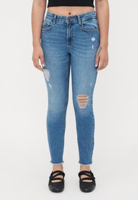 Skinny jeans in light blue denim with distressed details, featuring frayed hem and rips on the knees. Paired with black flats.