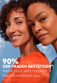 Two women with curly hair, one in a bright orange top, the other in a turquoise top, against a blue sky background.