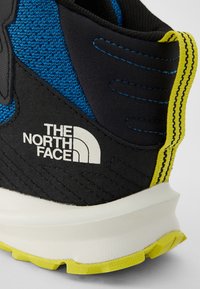 Baskets noires et bleues avec une tige texturée, accents jaunes et logo blanc. Présente une épaisse semelle blanche avec un motif de semelle robuste.