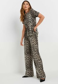 Top con stampa leopardata e pantaloni a palazzo in beige e nero. Il tessuto ha una texture liscia, con un dettaglio in vita annodato. Le scarpe nere completano l'outfit.