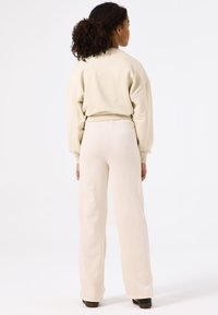 Licht beige sweatshirt met oversized mouwen, gecombineerd met crèmekleurige, geribbelde wijde broeken; zachte textuur, ontspannen pasvorm, minimalistisch ontwerp.
