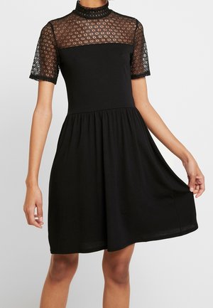 Schwarzes Kleid mit enganliegendem Oberteil und weitem Rock, mit kurzen Spitzenärmeln und Spitzenbesatz mit kreisförmigen Mustern und hohem Ausschnitt.