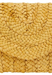 Knytväskan i vävd halm har en strukturerad yta och en mjuk gul färg, med ett cirkulärt mönster som skapar visuell djup.