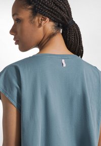 Blå bomulds-T-shirt med løs pasform, med korte ærmer og en lyserød mærkeetiket i nakken bagpå. Blød tekstur.