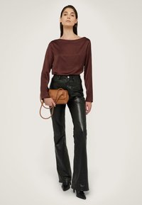 Blusa marrone a maniche lunghe, pantaloni in pelle neri a vita alta e svasati, e borsa color sabbia. Tessuto lucido e design aderente con cuciture visibili.